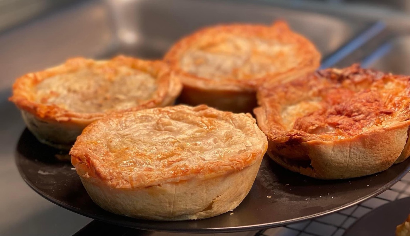 Four golden pies on a dark tray in the cabinet