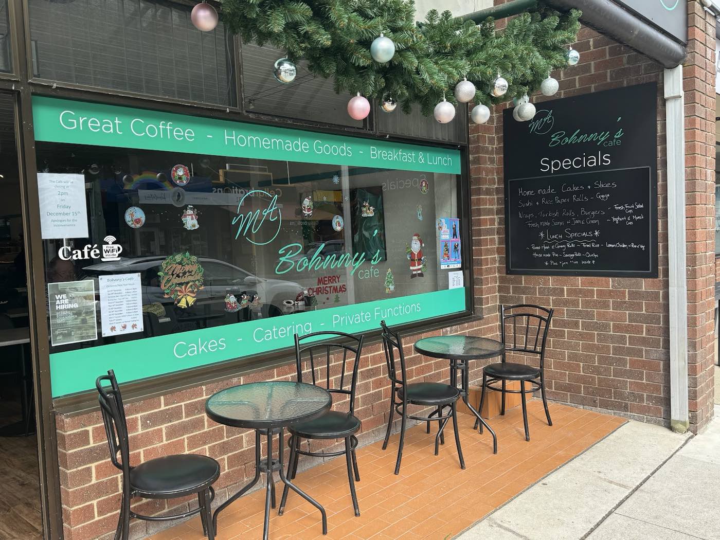 The shopfront: a green sign band across the window reading Great Coffee, Homemade Goods and Breakfast and Lunch, a Specials chalkboard, and small cafe tables on the footpath